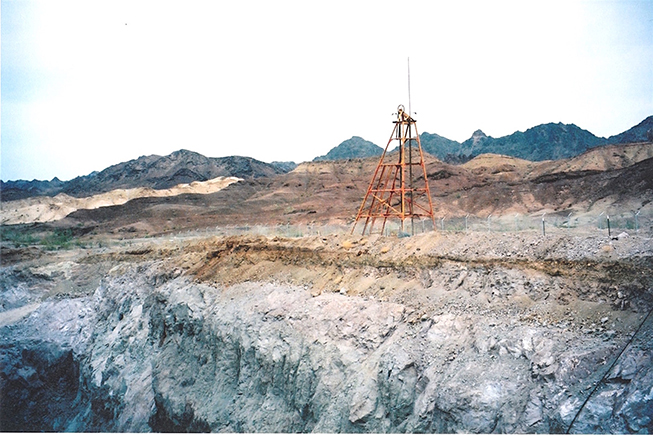 View of main mine shaft, outside the chain link fence. Open pit in foreground. View to the north-east